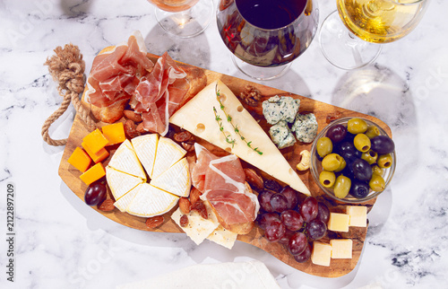 Cheese and charcuterie board with various meats, cheeses, nuts, and grapes on a marble table