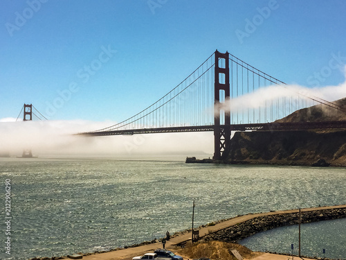 The Golden Gate Bridge, partially shrouded in fog, under a clear blue sky.
