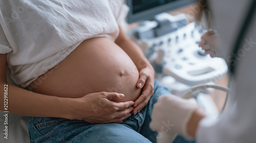 Pregnant woman cradles her belly during a prenatal ultrasound examination in a modern medical clinic.
