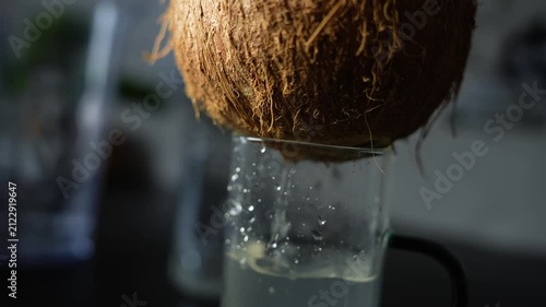 Close-up of a coconut dripping fresh liquid into a glass on a dark background, Coconut dripping liquid into glass
