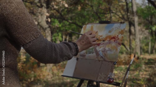 An artist at an easel in the park paints an autumn landscape in watercolor