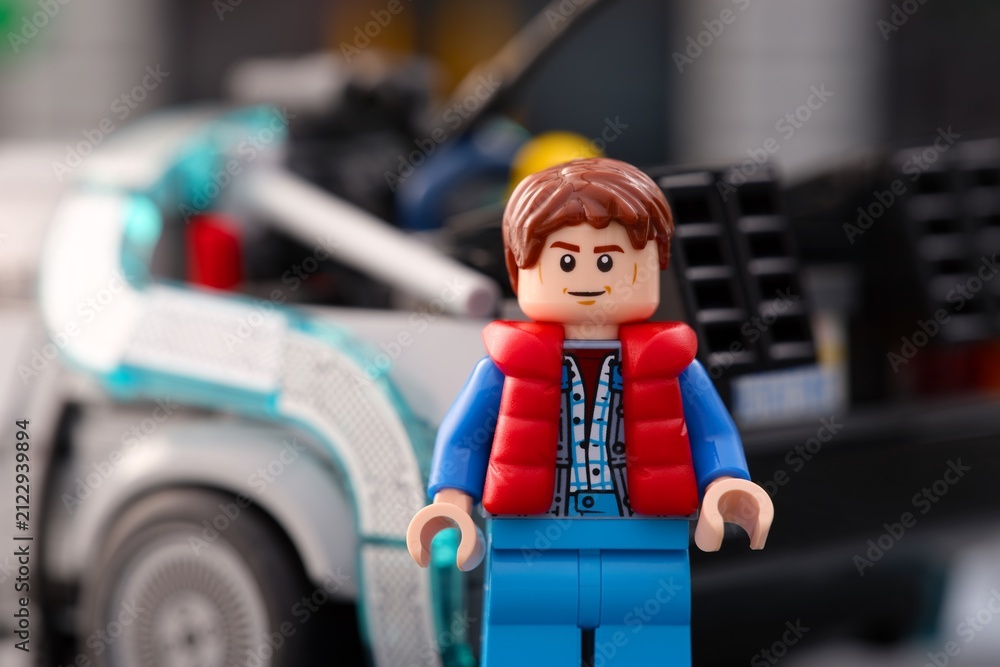 Fototapeta premium Tambov, Russian Federation - July 30, 2026 Portrait of a Lego Marty McFly minifigure standing near DeLorean time machine car from Back to the Future.