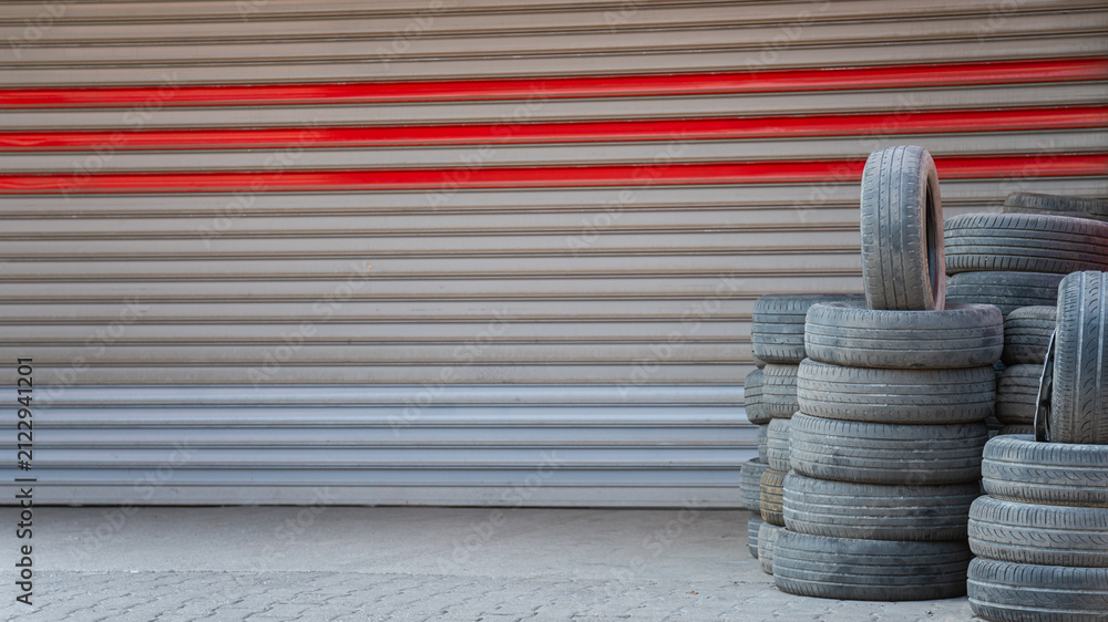 Obraz premium Stack of Used Car Tires Standing Against Industrial Roller Shutter Door
