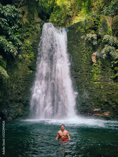 Young man enjoying refreshing swim in natural waterfall pool. Sao Miguel, Azores.
