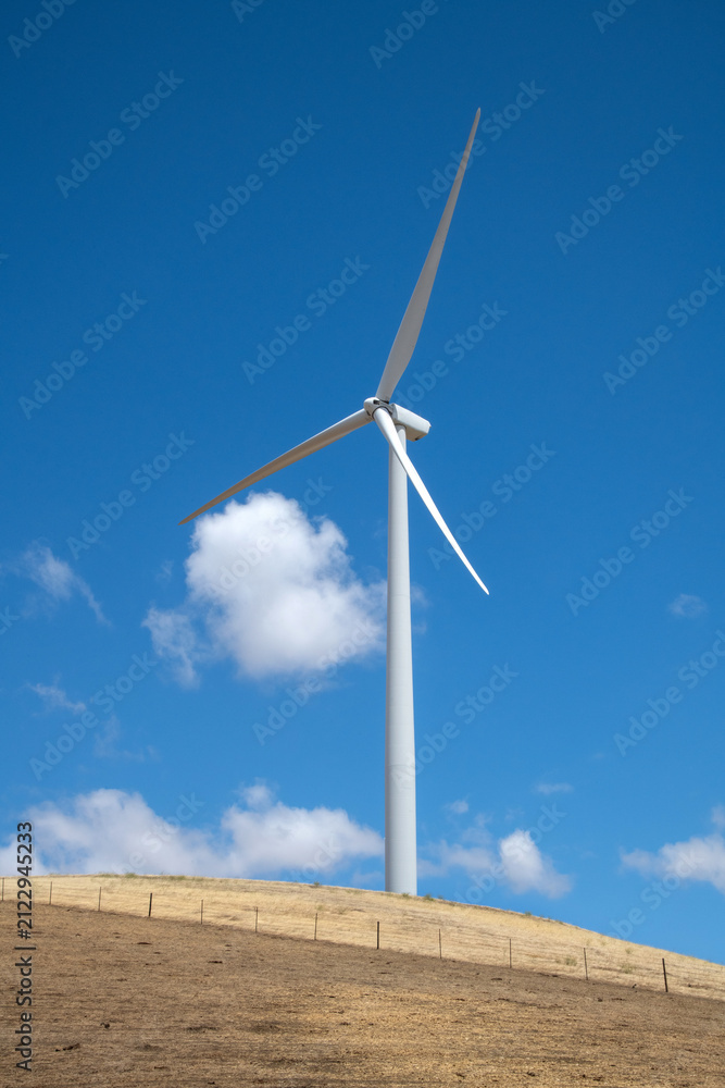 Fototapeta premium Tall Wind Turbine Stands Against a Clear Blue Sky, Capturing Renewable Energy on a Sunny Day