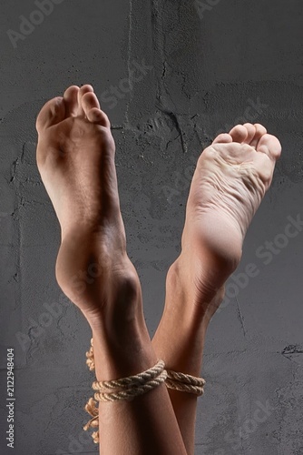 Close-up of a person's bare feet and ankles bound with thick rope
