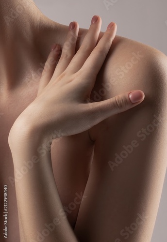 Intimate close-up of a woman's gentle hand on her bare shoulder.