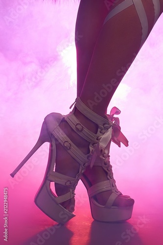 Woman's legs in strappy platform stiletto heels with pink neon backlighting and smoke