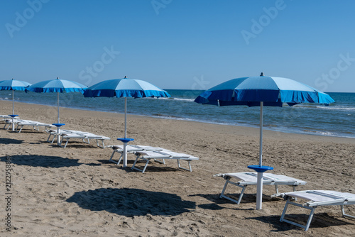 Fotografie Blue beach umbrellas and empty sunbeds line on sandy shore near Sperlonga, Italy