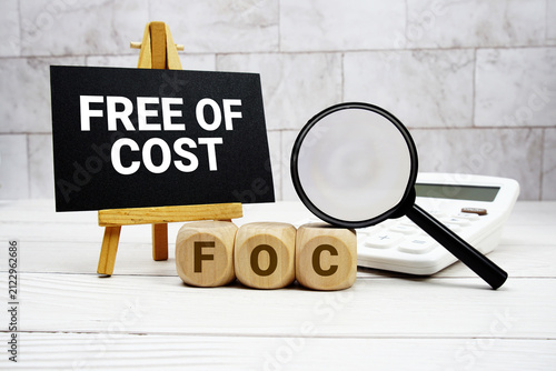 Fotografie FOC Free Of Cost text with calculator magnifying glass and on wooden background