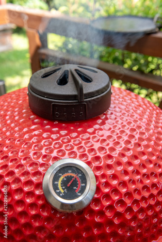 ceramic kamado grill with adjustable top vent releasing hot smoke
