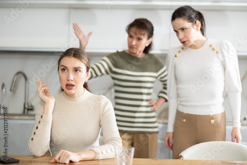 фотографія Upset middle-aged woman sitting at the kitchen table with her back to women quar