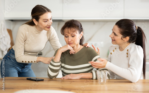 Fotografie Two middle-aged ladies consoling their friend which looks sorrowful sitting at t