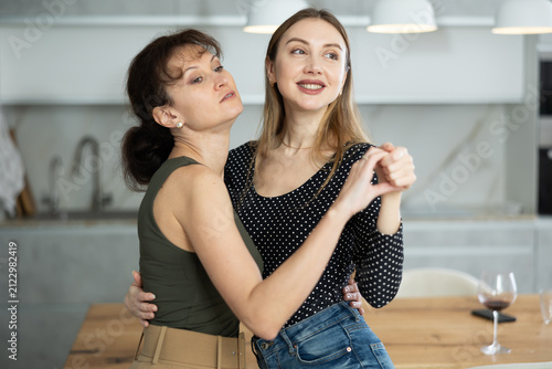 Bild auf Leinwand Two joyful middle-aged women dancing together at the table with wineglasses in l