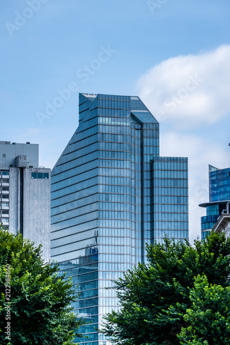 Distinctive modern glass office building rising above green trees in Brussels, blending contemporary architecture, sustainable urban scenery and expansive blue sky with copy space for designers.
