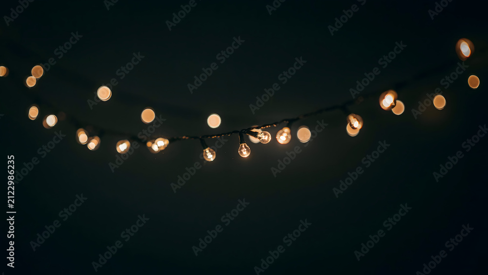 Obraz premium A string of warm glowing fairy lights hanging against a dark background, creating a soft bokeh effect for festive holiday atmosphere