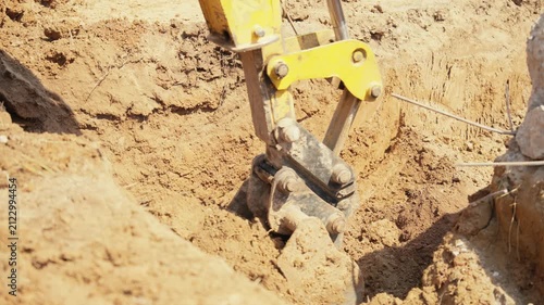 Heavy machinery with a mechanical shovel digging a hole in the ground during earthmoving works at a construction site, preparing the foundation for a new building in sunny daylight