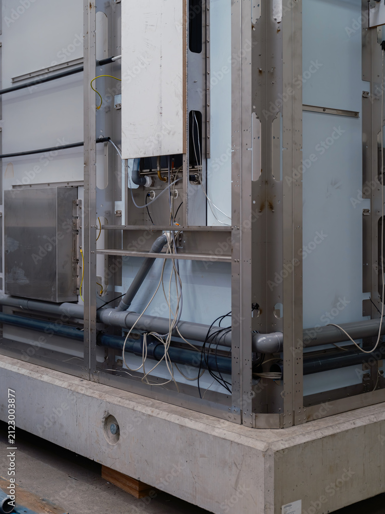 Fototapeta premium A corner of a prefabricated module with a steel frame, pipes and cabling on a concrete base.