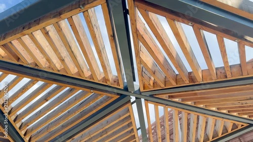 Architectural wooden structure with triangular beams and metal framework, showcasing the intricate design of a modern canopy against a clear blue sky