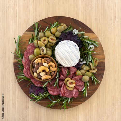 Overhead view of a timber gourmet charcuterie board or cheese platter with various meats, olives, nuts and cheese 