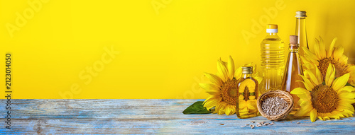 Rural still-life, banner - sunflower oil in bottles with flowers of sunflower (Helianthus annuus), closeup with space for text