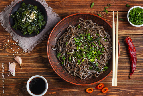 Still life with top view of traditional japanese soba noodles with nori (edible seaweed) and soy sauce, on a wooden surface closeup