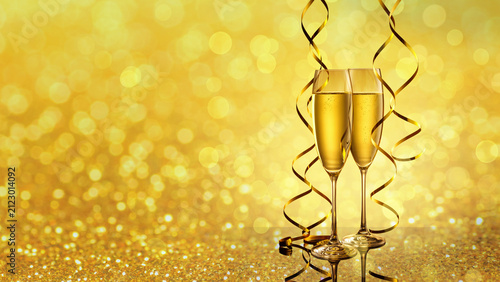 Two elegant perfect glasses filled with carbonated drink or sparkling champagne with golden serpentines on golden shiny background. Christmas, New Year, anniversary, holiday horizontal background