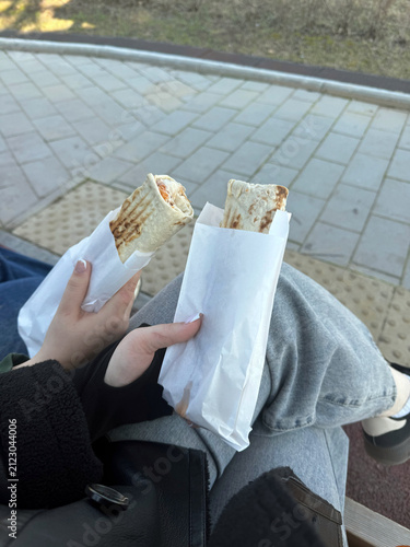 Bild auf Leinwand Two hands holding wrapped burritos while seated on a bench