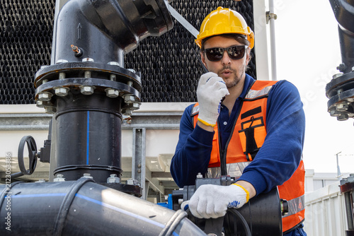 Obraz na plátně Industrial engineer with radio communicator inspecting factory cooling tower pipelineMaintenance technician in a hard hat and safety vest checking water valve pipesCaucasian supervisor monitoring