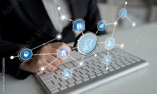 Fotografie A business professional uses a magnifying glass to analyze data while surrounded by digital icons, emphasizing technology, research, and communication in a modern workspace