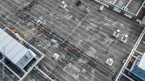 Aerial photo of two parallel HVAC, two pipe, heating and cooling black metal pipes with red elbow joints that are supported by metal frames on a flat rooftop.
