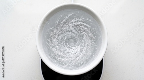 Top view whirlpool of clear hydrogen water inside white ceramic cup on light surface