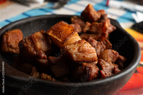 Deep fried pork belly bites served in a rustic black clay bowl close up