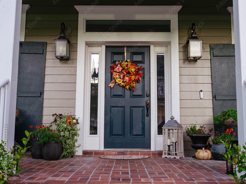Obraz premium A colorful autumn wreath hangs on the front door of a modern residential home. Seasonal flowers, pumpkins, and decorative plants create a warm fall entrance.