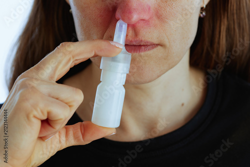 Foto A mid-adult woman applies a nasal spray to treat a blocked nose and irritated skin, demonstrating self-care and home treatment for cold and allergy symptoms