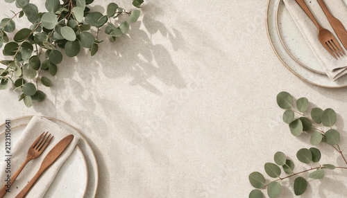 Aesthetic table setting with eucalyptus branches and wooden cutlery on neutral linen background.
