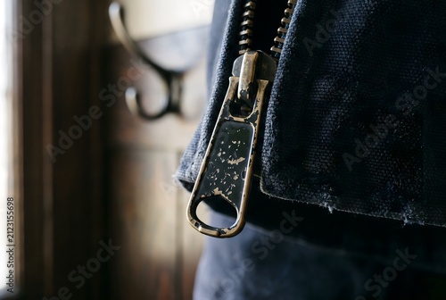 Macro close up of a metal zipper pull tab showing chipped paint and tarnished base metal