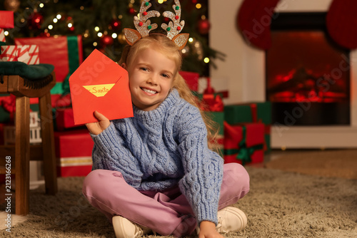 Cute little happy girl with envelope and letter to Santa sitting on floor in ...