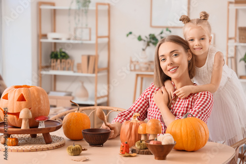 Cute little girl hugging her mother while carving Halloween pumpkins at home