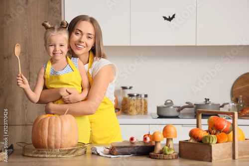 Cute little girl with her mother hugging while carving Halloween pumpkin in k...