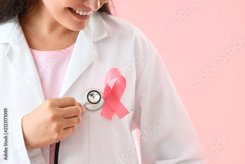Female doctor with pink ribbon on color background, closeup. Breast cancer aw...
