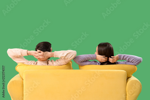 Beautiful young couple resting on sofa against green background, back view