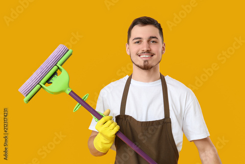 Male janitor with floor mop on yellow background