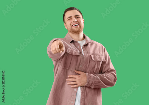 фотографія Laughing young man pointing at viewer on green background