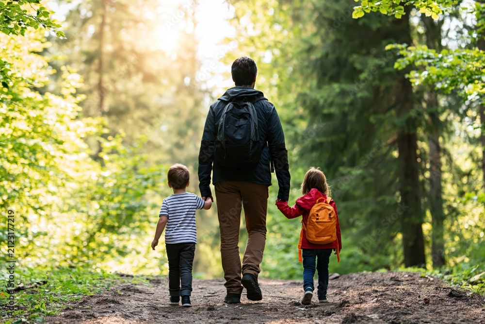 Obraz premium Father walking with his children and son daughter hiking in a sunny forest nature