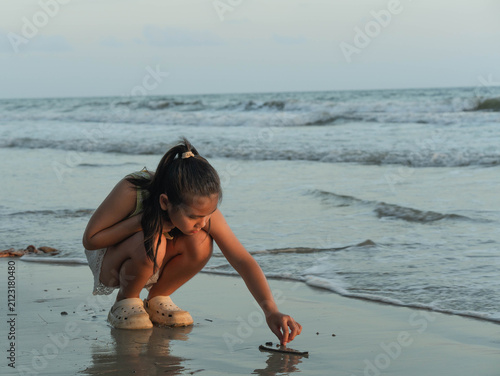 Картината върху платно Asian girl crouching down drawing and writing on wet sand at beach shore with oc
