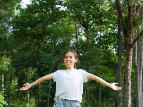 Happy young Asian girl standing with open arms enjoying fresh air and green trees in a summer forest