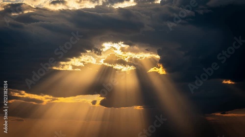 Dramatic sunlight rays breaking through dark storm clouds creating golden sky at sunset