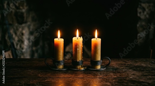 Three candles burn brightly on a wooden table. The candles are in metal holders.