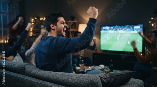 Side-rear view of a man celebrating a goal during a soccer game on a couch.